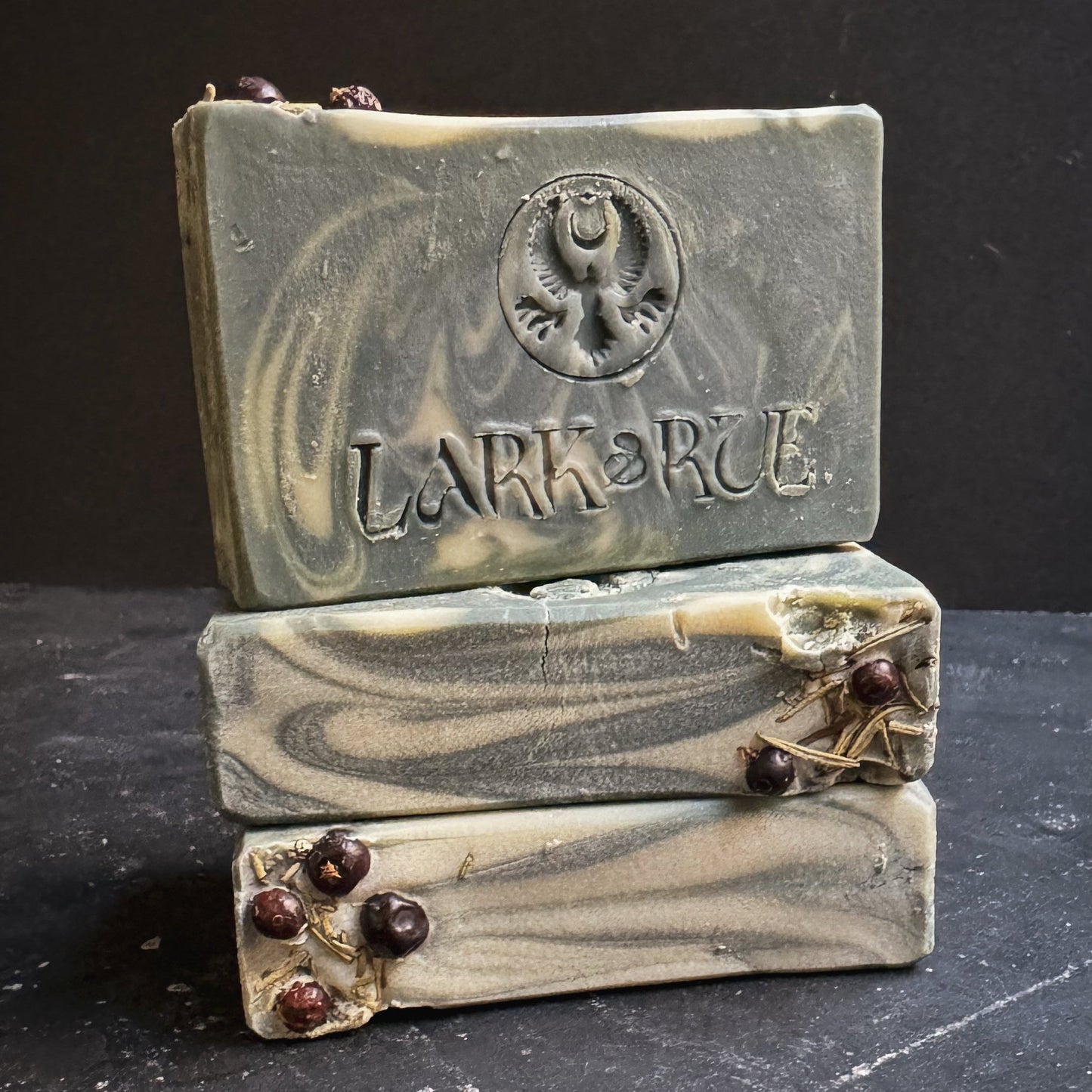 Image of 3 stacked green and white swirled soap bars. the top bar is stamped with the Lark & Rue logo