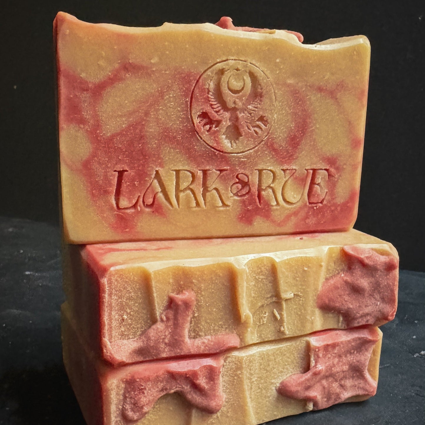 Image of 3 soap bars with white and red swirls. The top soap is stamped with the Lark & Rue logo.