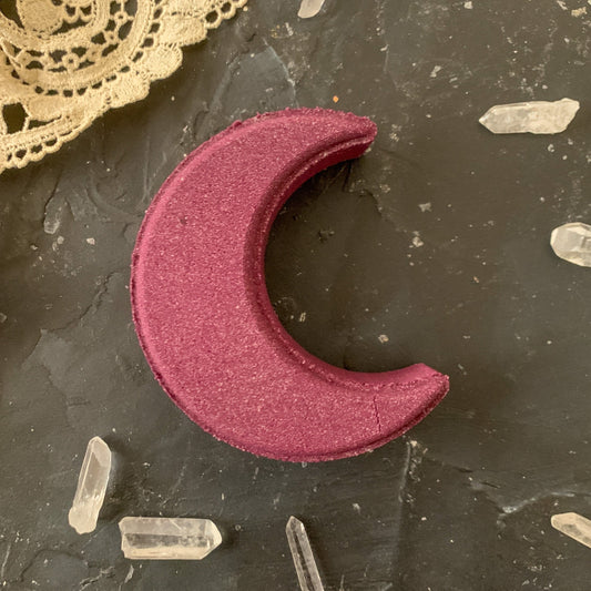 Image of a deep purple crescent moon bath bomb sourrounded by crystals and lace