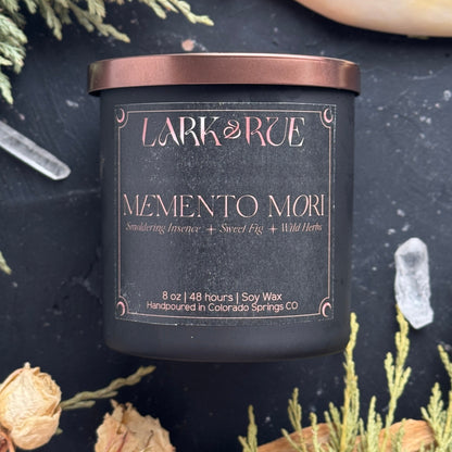 Memento Mori candle on dark background with dried cedar and roses.
