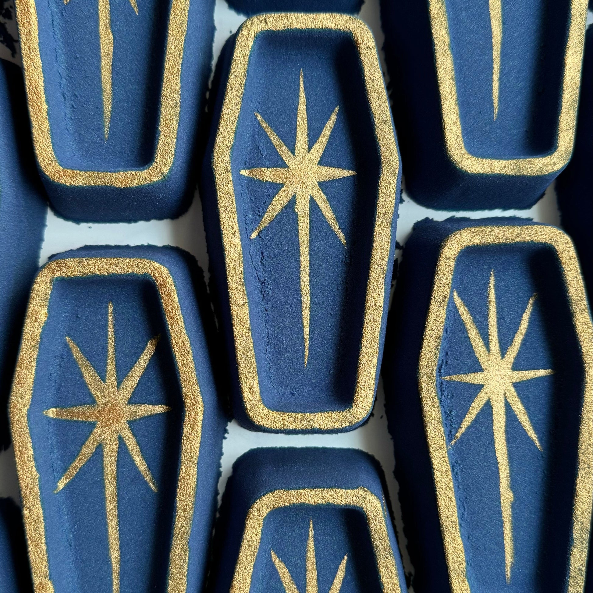 Image of several dark blue coffin shaped bath bombs with hand-painted edge details and a Lage star in the center.