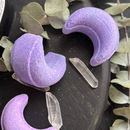 Image of light purple crescent moon shower steamers on dark background with quartz crystal points and dried eucalyptus leaves.