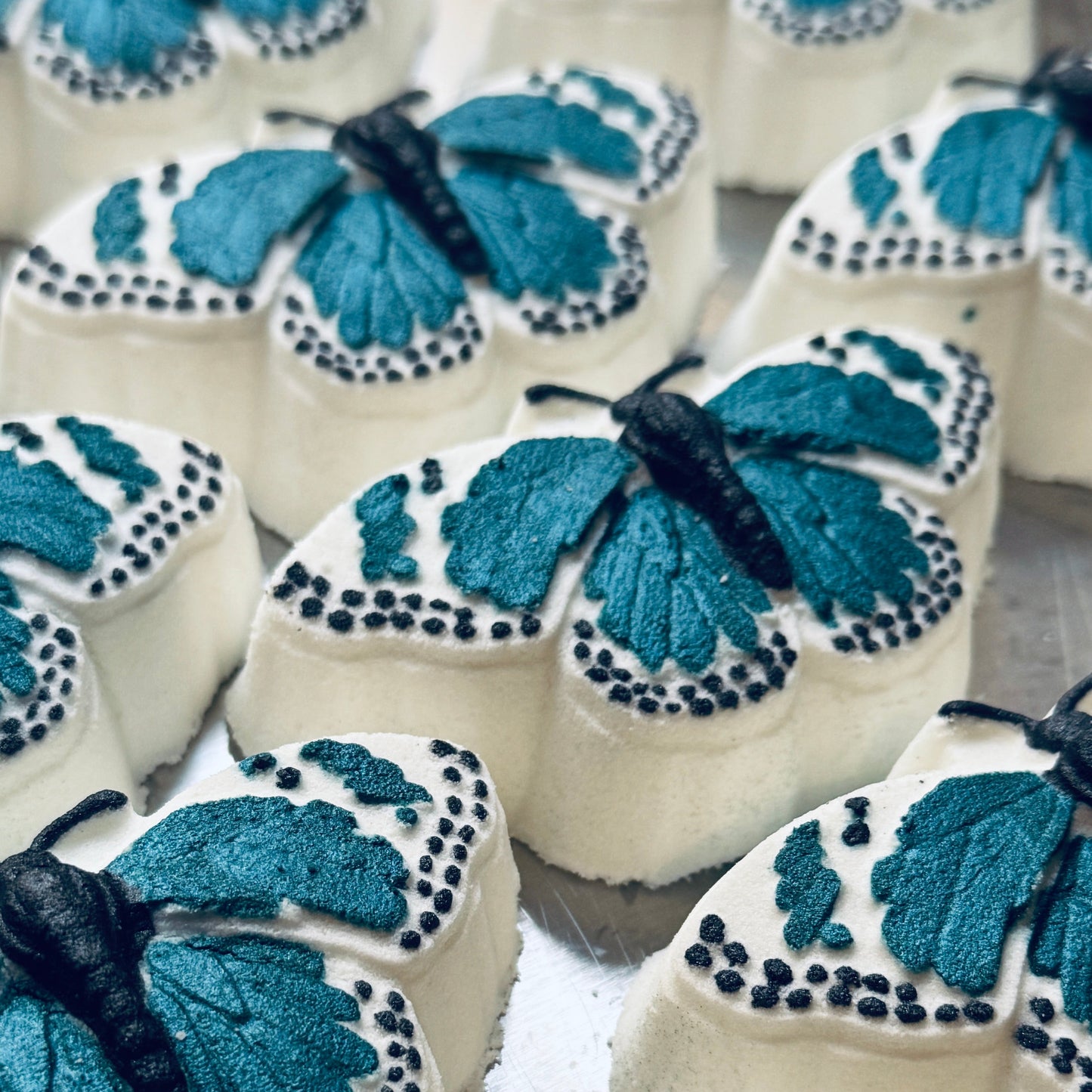 Image of white butterfly bath bombs with wings painted a dark teal and black.