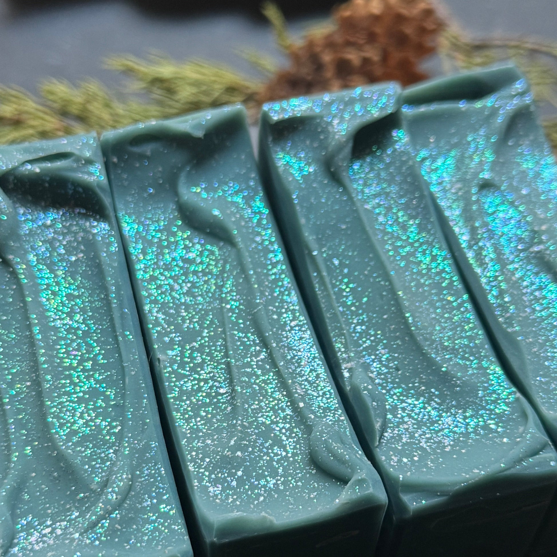 Siren Song soap top gentle waves covered in blue/green/silver color shift shimmer with natural elements in background.